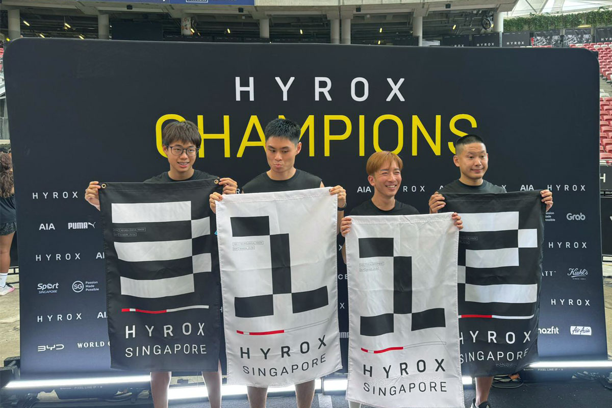 Four smiling adaptive athletes proudly holding up HYROX Singapore champion flags at the National Stadium backdrop.
